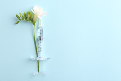 Photo of Cosmetology. Medical syringe and freesia flower on light blue background, top view. Space for text