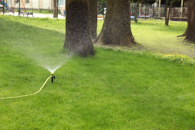 Photo of Automatic sprinkler watering green grass in park