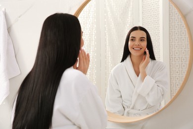 Photo of Beautiful young woman in bathrobe near mirror indoors