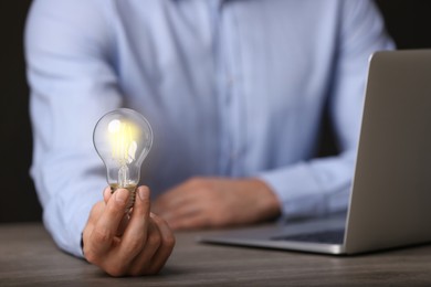 Photo of Glow up your ideas. Closeup view of man holding light bulb while working at wooden desk, space for text