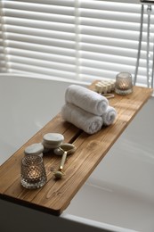 Wooden tray with spa products and burning candles on bath tub in bathroom