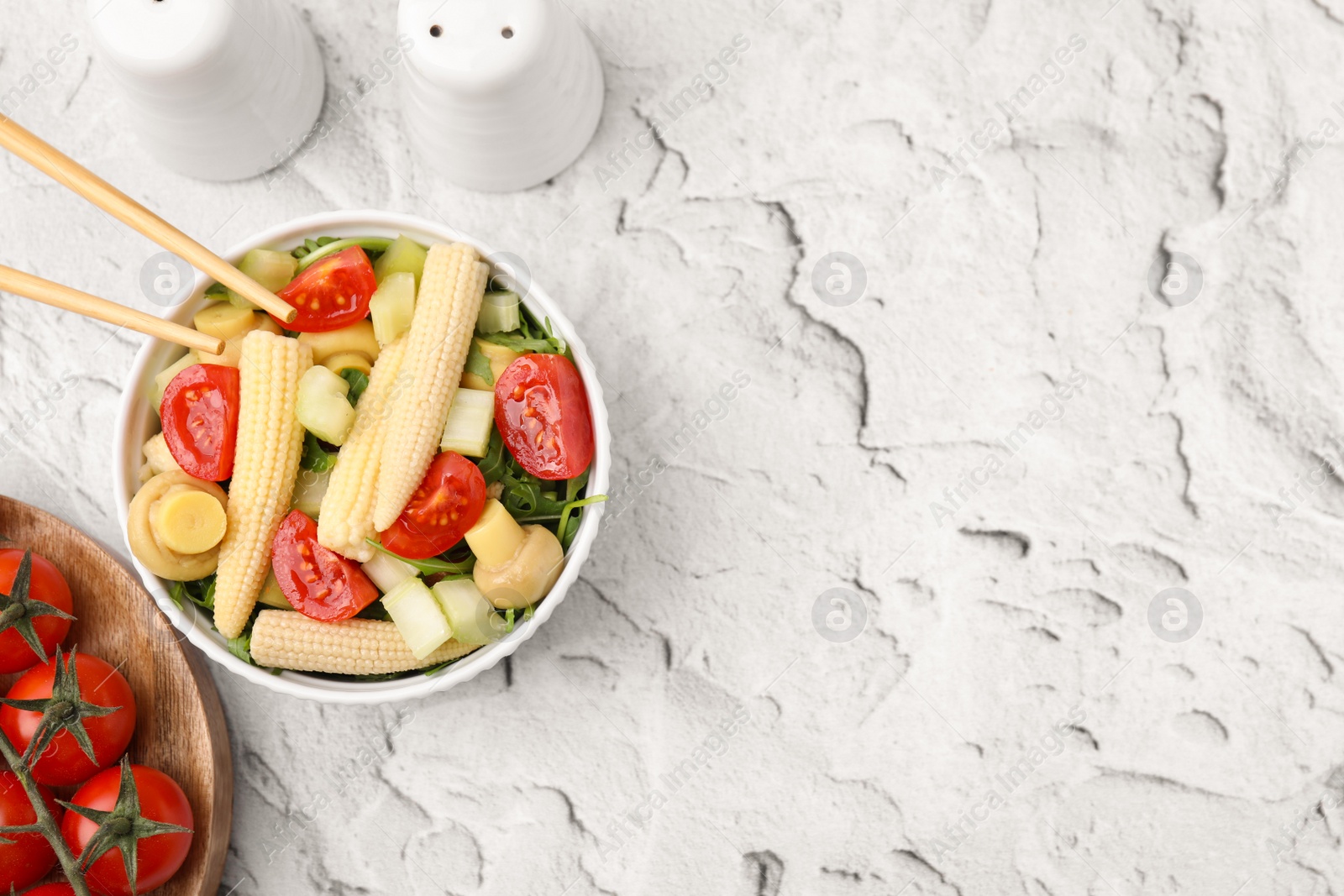 Photo of Tasty baby corn with vegetables and champignons on grey textured table, flat lay. Space for text