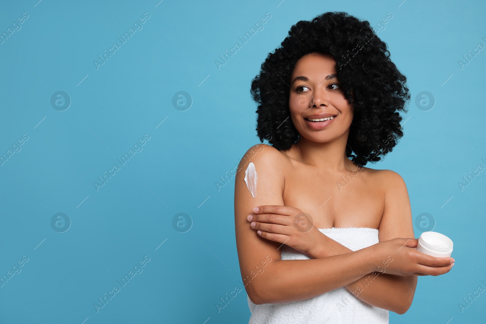 Photo of Young woman applying body cream onto shoulder on light blue background. Space for text