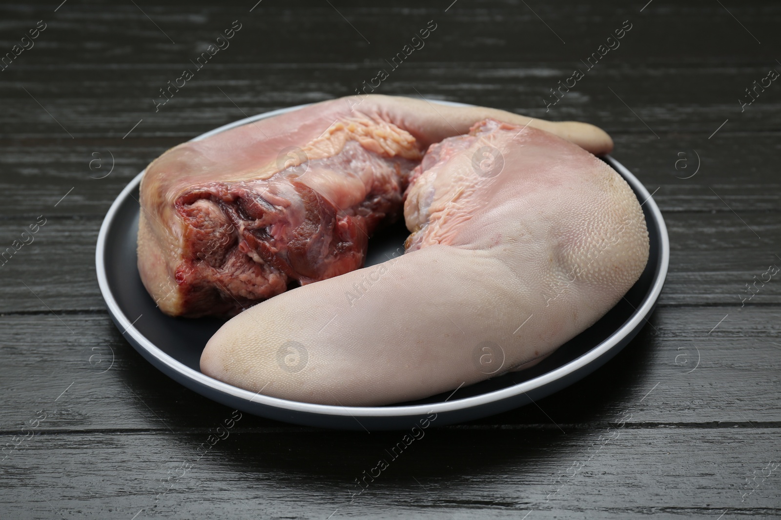 Photo of Plate with raw beef tongues on black wooden table, closeup
