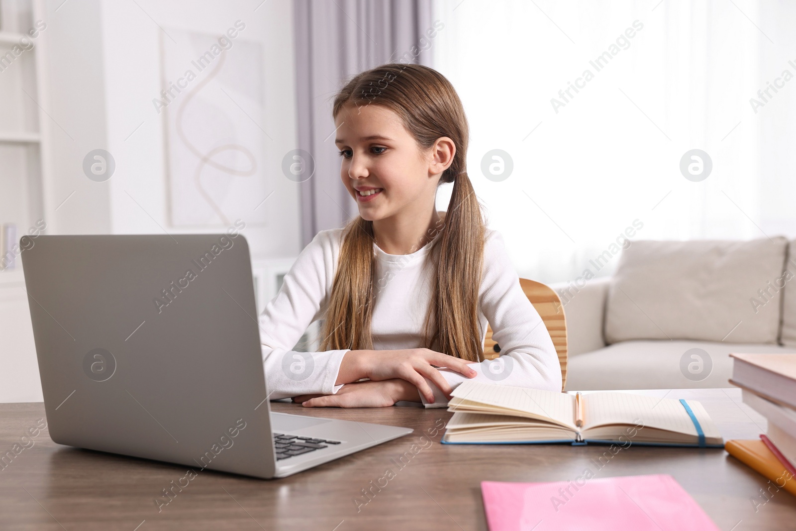 Photo of E-learning. Cute girl using laptop during online lesson at table indoors