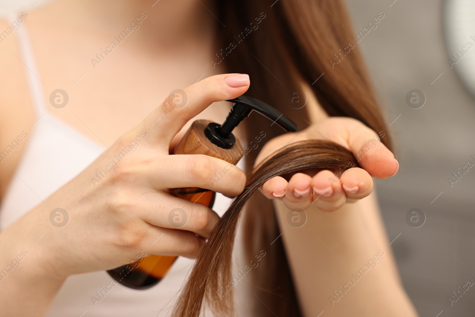 Photo of Woman applying oil hair mask indoors, closeup