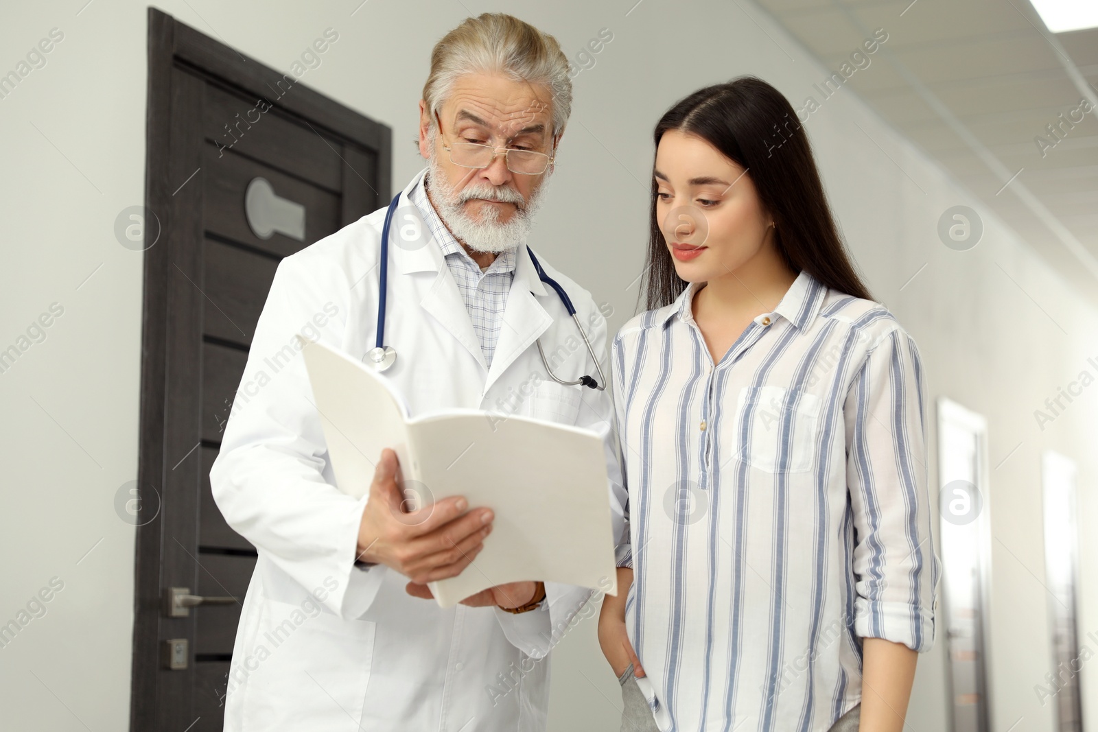 Photo of Senior doctor with notebook consulting patient in clinic