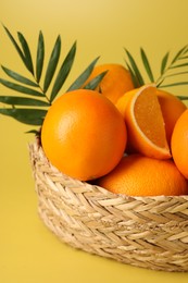 Photo of Fresh oranges in wicker basket on yellow background, closeup