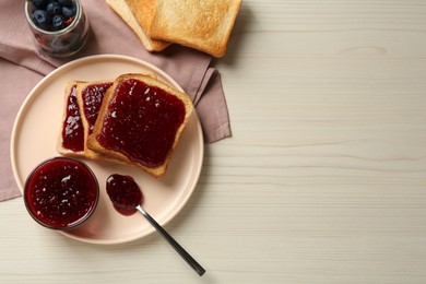 Photo of Delicious toasts served with jam and berries on white wooden table, flat lay. Space for text