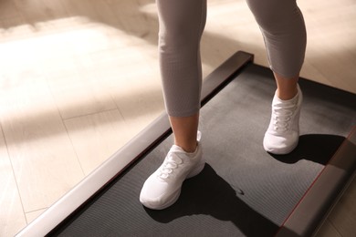 Photo of Sporty woman training on walking treadmill indoors, closeup