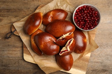 Photo of Delicious baked cranberry pirozhki on wooden table, flat lay