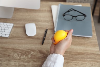 Man squeezing yellow stress ball in office, closeup