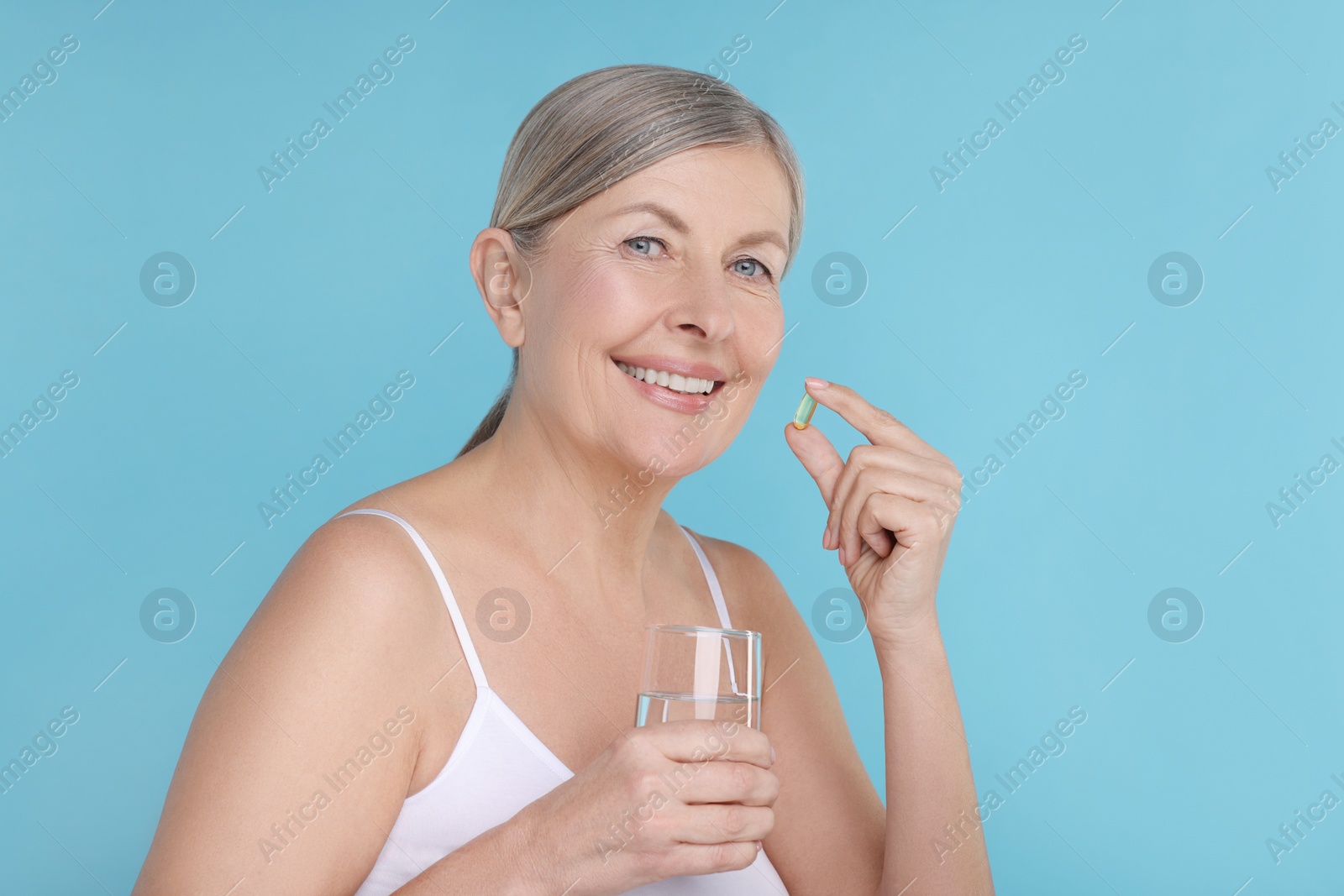 Photo of Beautiful woman with vitamin capsule and glass of water on light blue background