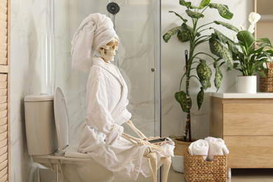 Skeleton in bathrobe with mobile phone sitting on toilet bowl