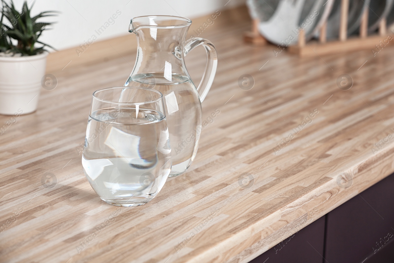 Photo of Glass and jug with fresh water on table in kitchen. Space for text