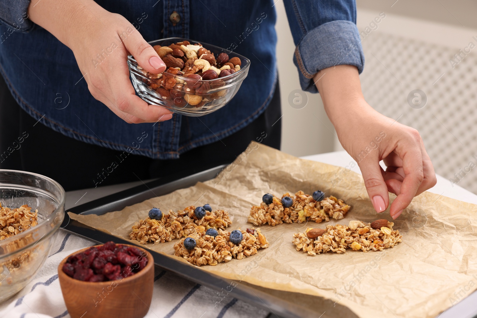 Photo of Making granola bars. Woman with nuts at table in kitchen, closeup