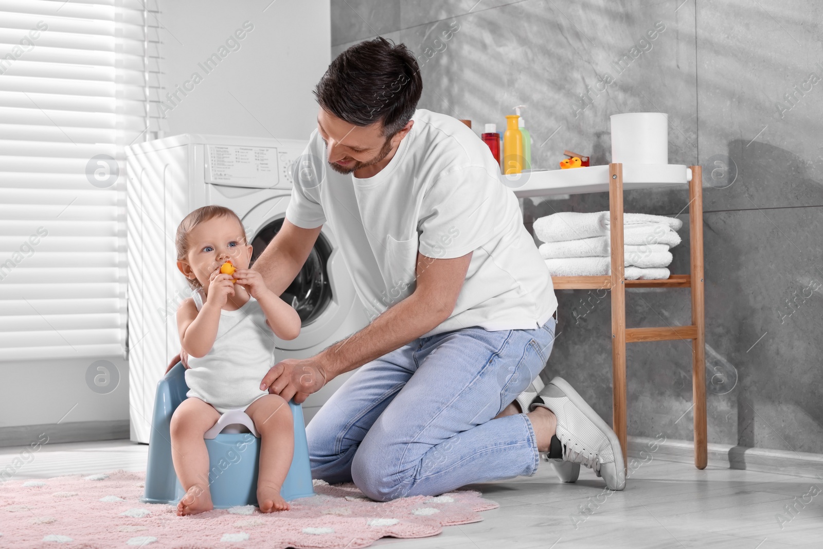 Photo of Father training his child to sit on baby potty indoors