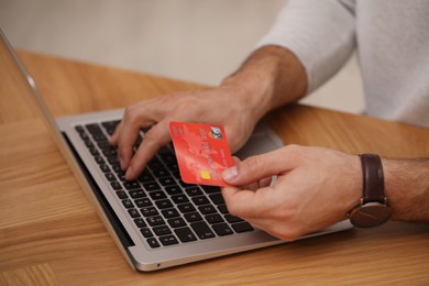 Man using laptop and credit card for online payment at wooden desk, closeup