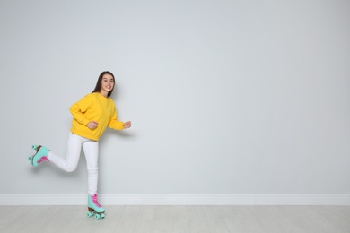 Photo of Young woman with roller skates near color wall. Space for text