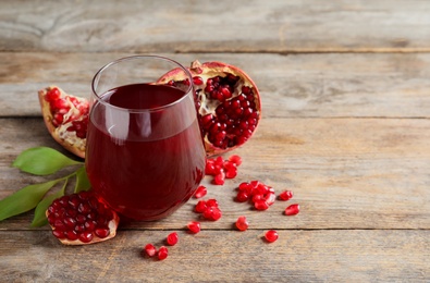 Photo of Glass of pomegranate juice and fresh fruits on wooden background, space for text