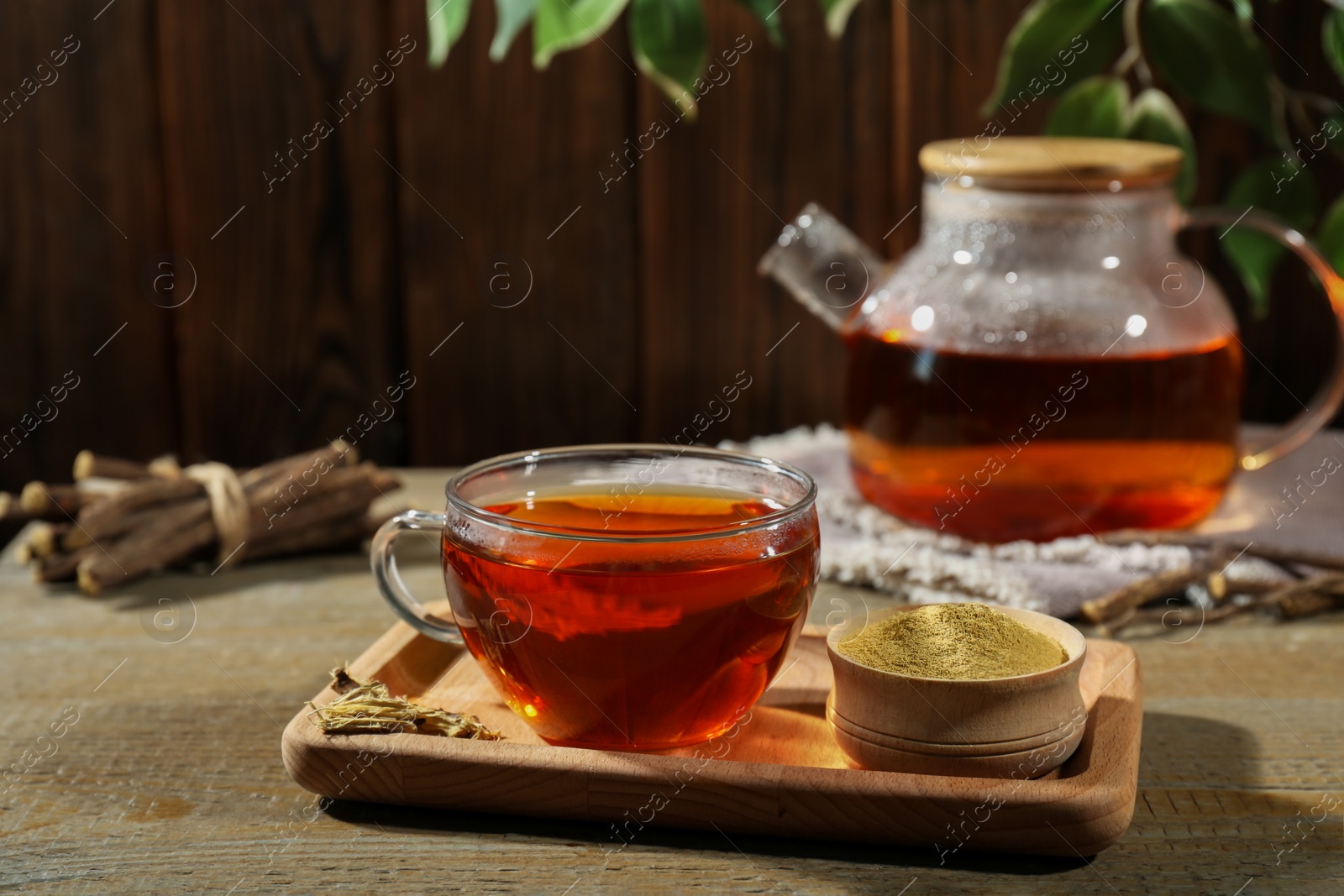 Photo of Aromatic licorice tea in cup and powder on wooden table, space for text