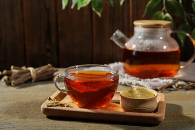 Aromatic licorice tea in cup and powder on wooden table, space for text