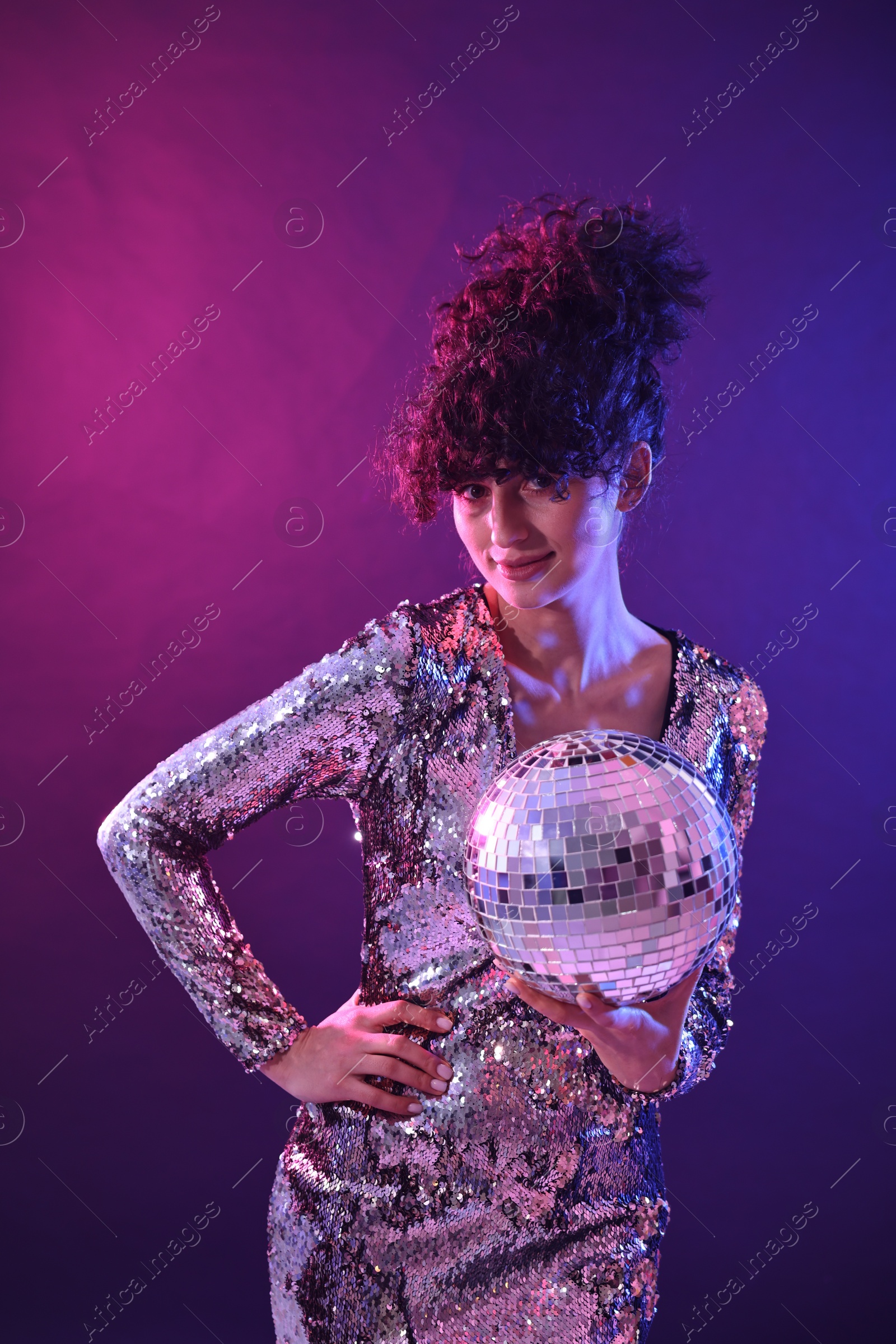 Photo of Beautiful young woman with disco ball posing on color background in neon lights