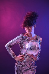 Beautiful young woman with disco ball posing on color background in neon lights