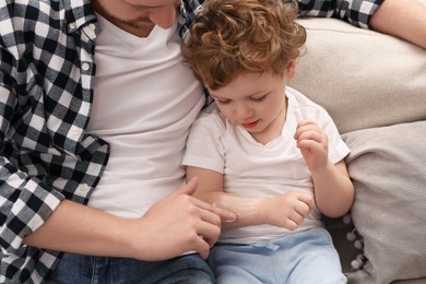 Photo of Father applying ointment onto his son`s arm on sofa