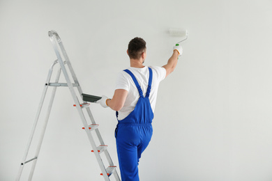 Man painting wall with white dye indoors, back view