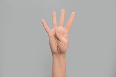 Photo of Woman showing number four on grey background, closeup. Sign language