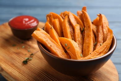 Photo of Bowl with tasty sweet potato fries on wooden board