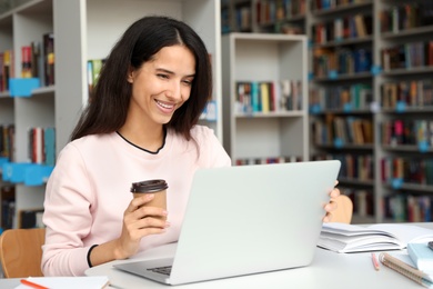 Young happy woman using laptop at table in library