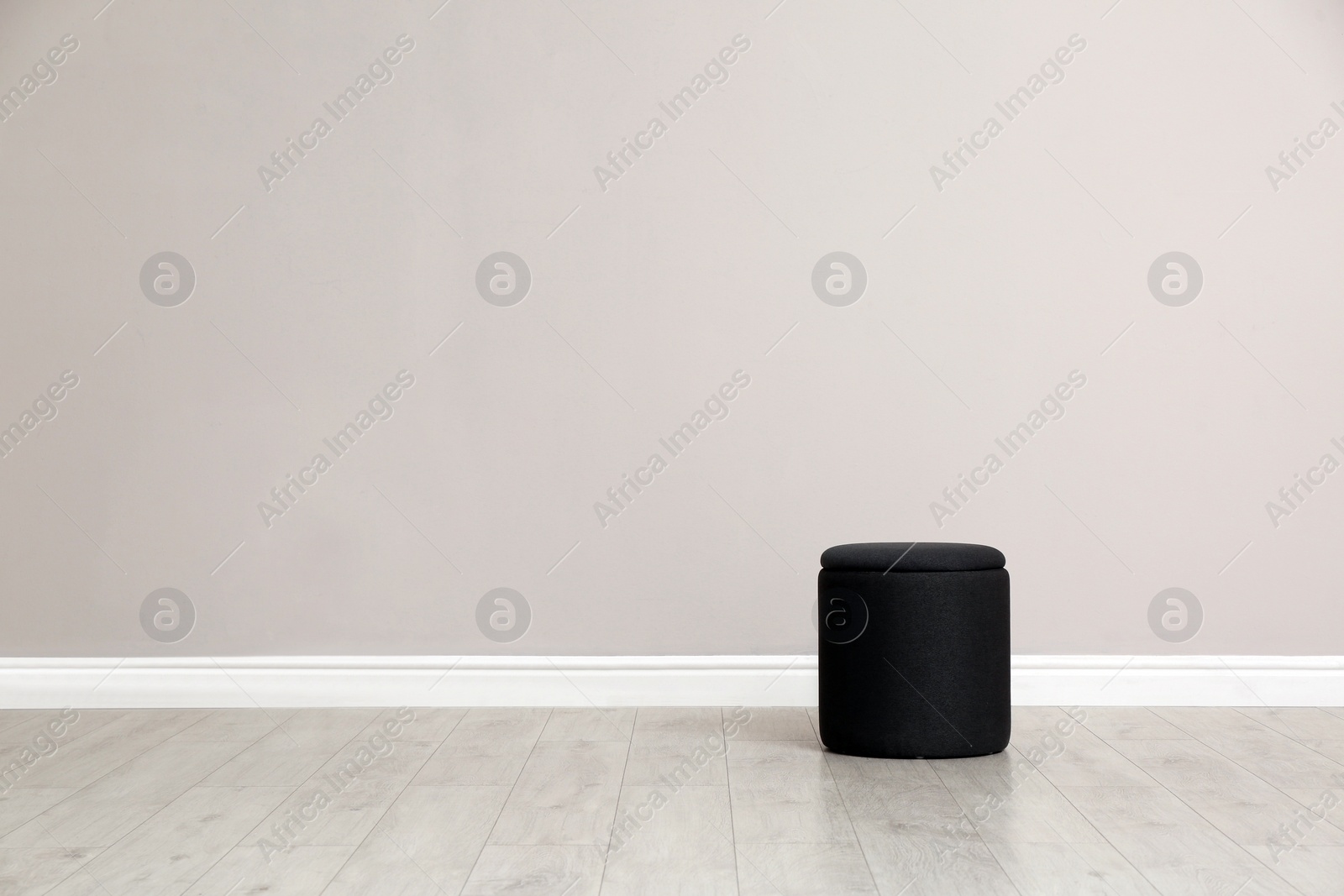 Photo of Stylish pouf near beige wall indoors. Space for text