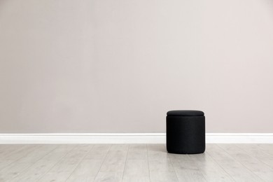 Stylish pouf near beige wall indoors. Space for text