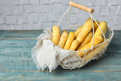 Photo of Many raw white carrots in metal basket on blue wooden table
