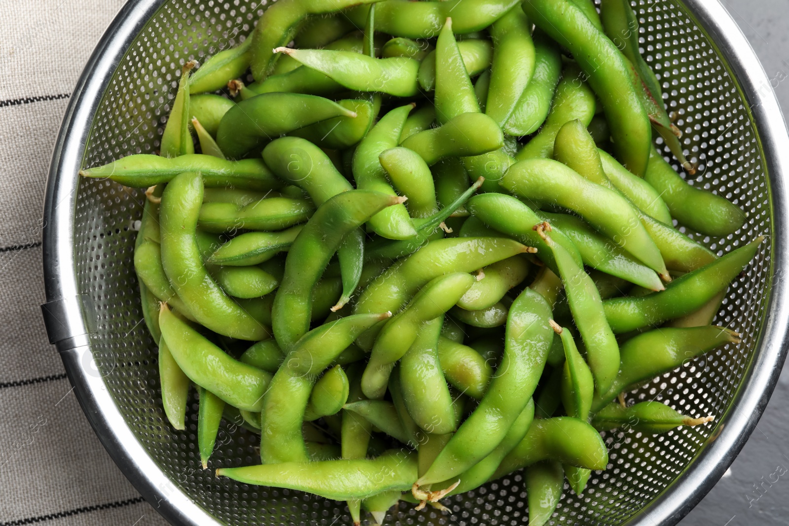 Photo of Sieve with green edamame beans in pods on table, top view