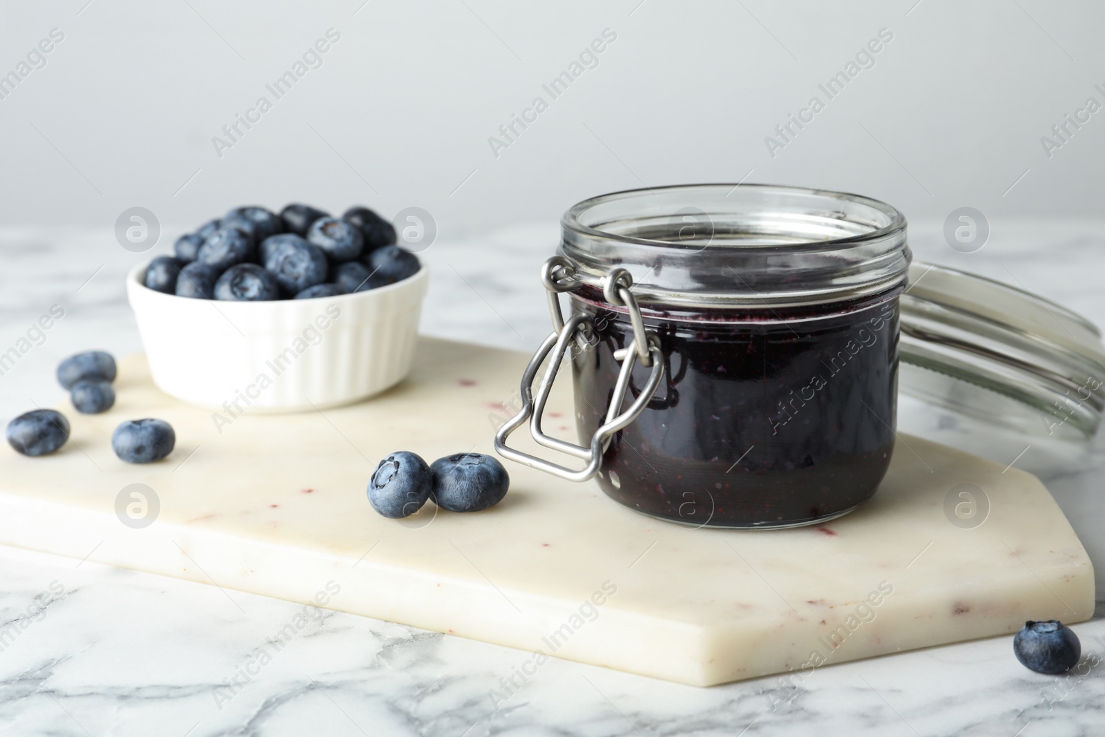 Photo of Jar of blueberry jam and fresh berries on white marble table