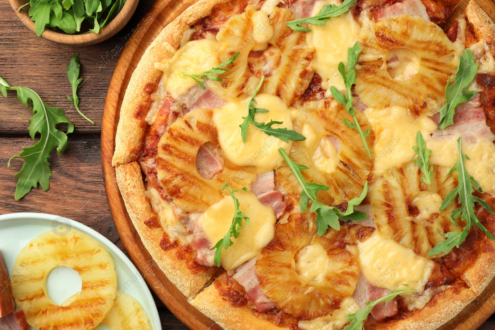 Photo of Delicious pineapple pizza and ingredients on wooden table, flat lay