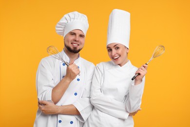 Happy professional confectioners in uniforms holding whisks on yellow background