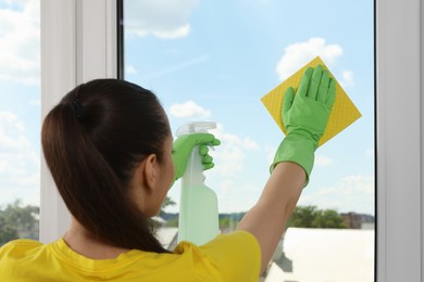 Photo of Woman cleaning window glass with sponge cloth and spray indoors