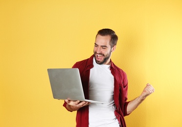 Photo of Emotional young man with laptop celebrating victory on color background