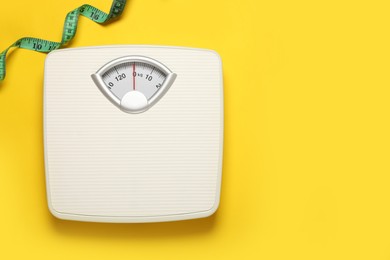 Photo of Weigh scales and measuring tape on yellow background, top view with space for text. Overweight concept