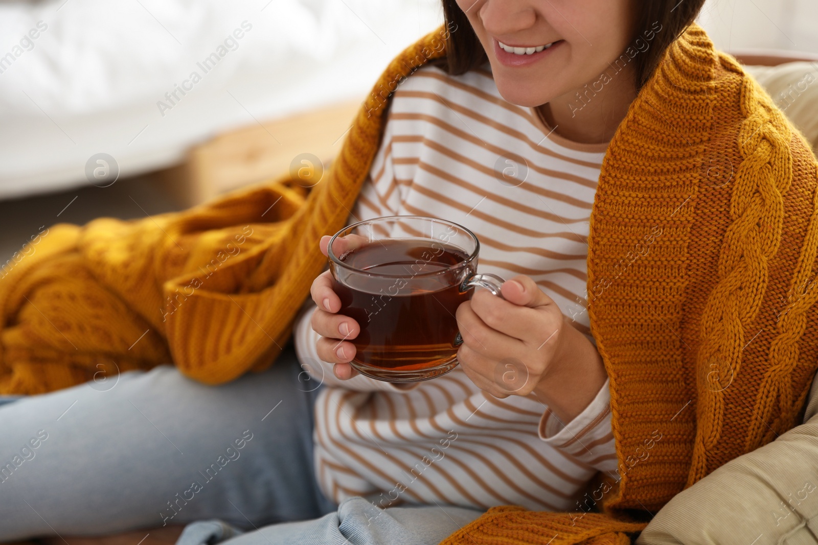 Photo of Woman covered with warm orange plaid enjoying hot drink at home, closeup