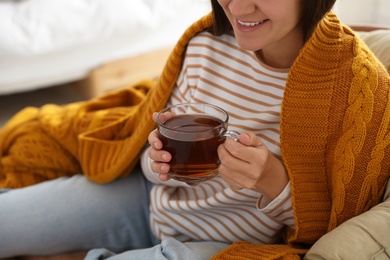 Woman covered with warm orange plaid enjoying hot drink at home, closeup