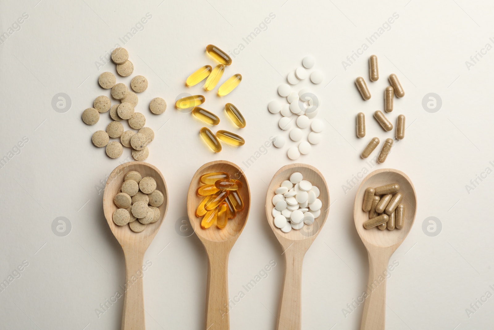 Photo of Wooden spoons and different dietary supplements on white background, flat lay