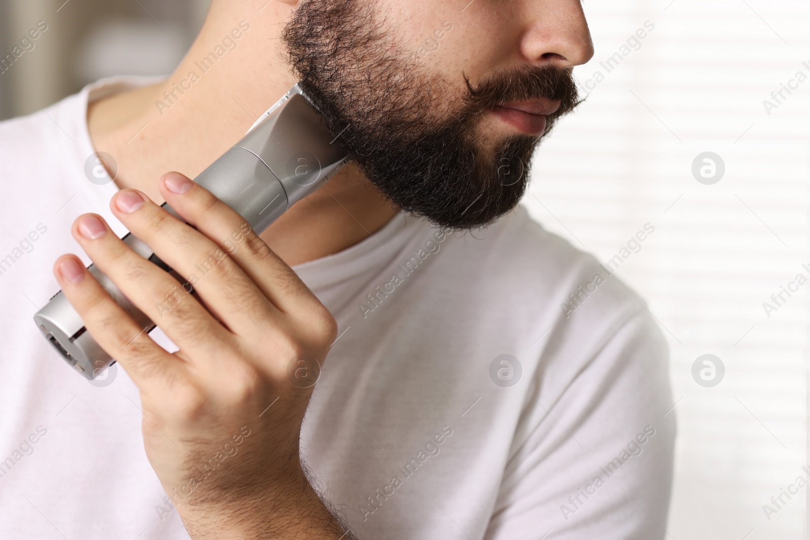 Photo of Handsome young man trimming beard at home