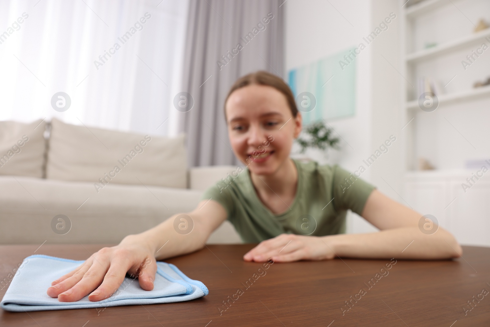 Photo of Woman with microfiber cloth cleaning wooden table in room, selective focus