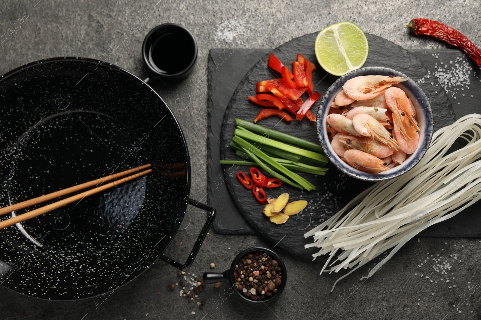 Photo of Flat lay composition with black wok, spices and products on dark textured table