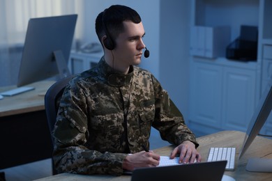 Military service. Young soldier in headphones working at wooden table in office at night